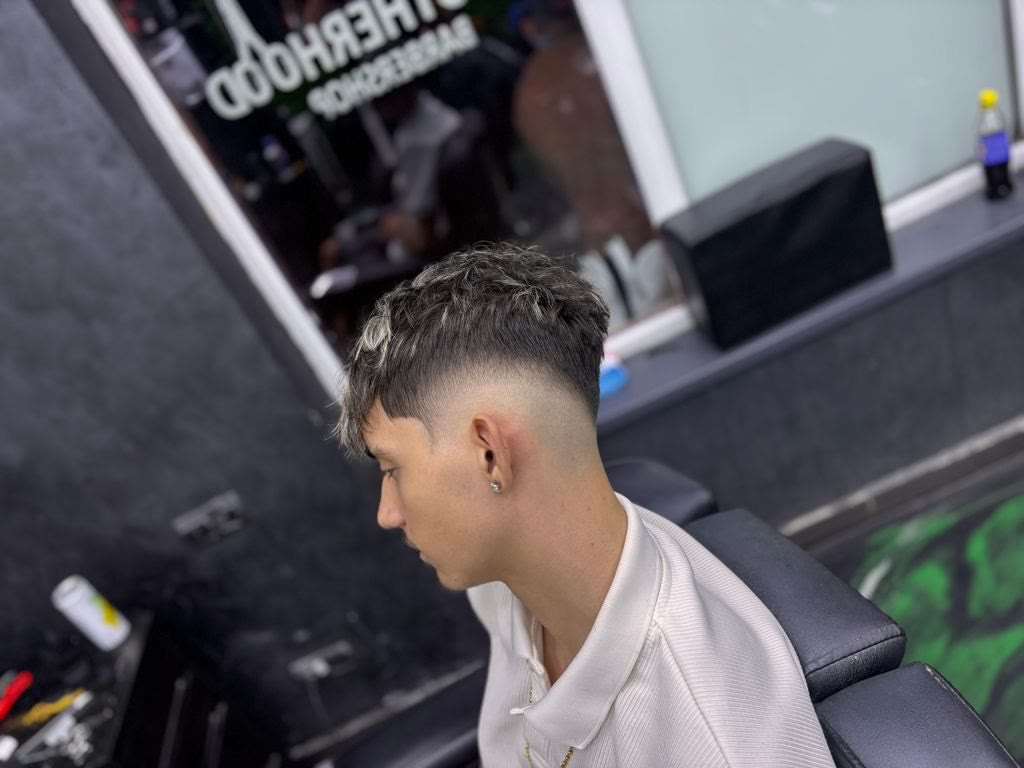 Client cu low fade, în fața oglinzii cu sigla salonului